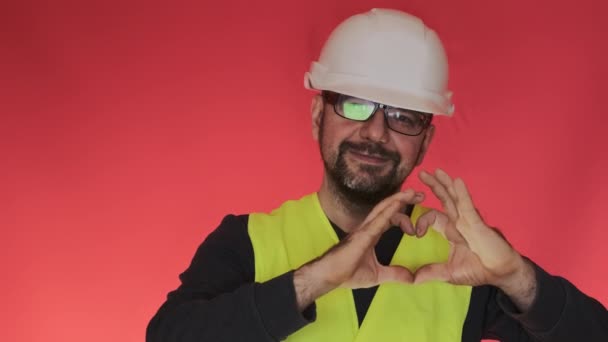 人物形象使人的心形 双手模仿红色背景下的跳动 戴头盔的戴胡子的工程师表现出爱情特写 — 图库视频影像