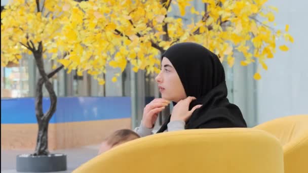 Muzułmanka Siedząca Żółtej Kanapie Naprawia Czarny Hidżab Chłopiec Maluch Rozgląda — Wideo stockowe