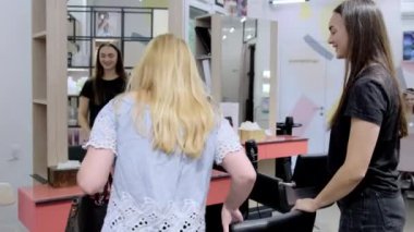 KYIV, UKRAINE - 27 Eylül 2021: Yazlık gömlekli uzun saçlı bayan koltukta oturmuş stilistten yeni saç stilini bekliyor. Profesyonel kuaför müşterilerinin saç kalitesini ölçüyor.