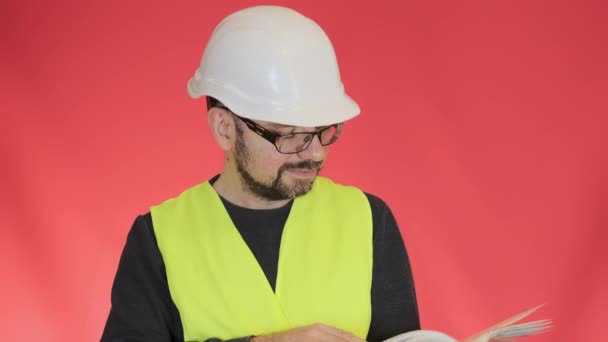 眼鏡のプロのエンジニアは ページを反転プロジェクト計画を承認します 髭の男で保護ヘルメットノード頭上の赤の背景クローズアップ — ストック動画