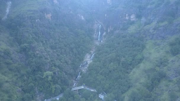 ラバナの滝は スリランカの熱帯島の霧深い山の熱帯林に流れています 滝の空中ビューを横断する橋の上に車を運転 — ストック動画