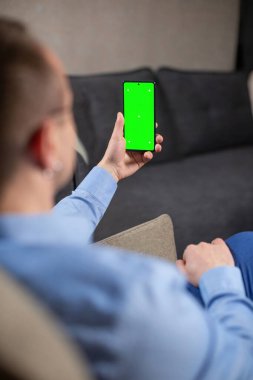 Mavi gömlekli psikolog, açık koltukta otururken elinde krom ekranlı cep telefonu tutuyor. Fotoğraf ya da video malzemesi eklemek için krom anahtar