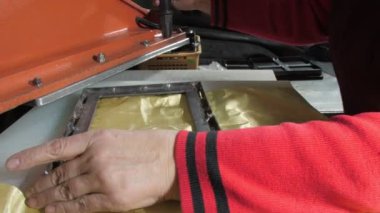 Eski imalat işçisi sarı metal kumaş üzerindeki kare metal bıçağı tamir ediyor ve tezgah presi ile kesiyor. Cüzdan zanaatı
