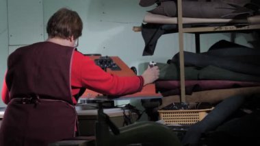 Terzi metal bıçağını kontrol eder. Deri kumaş giyer ve iş yerinde ağırlık kaldırır.