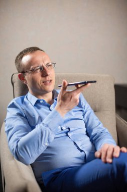 Gözlüklü erkek psikolog koltukta otururken cep telefonuyla konuşuyor. Erkek uzman iş yerindeki müşteriyi arar ve dinler.