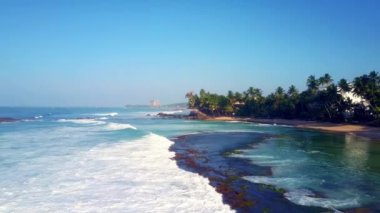 Okyanusun köpüklü dalgaları kumsaldaki kumu palmiye ağaçlarıyla kaplar. Adanın havadan görünüşü yavaş çekimde rahatlama ve doğayla bütünleşme kavramı
