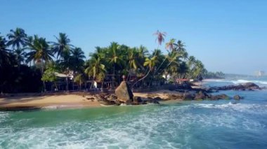 Turkuaz okyanus suları kayalık plajları turistlerle yıkıyor. Tropik yerlerdeki otellerde rahatlama kavramı yavaş çekim hava görüntüsü