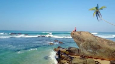 Turist huzursuz okyanus dalgalarıyla yıkanmış kayalarda oturur. Tropikal ada havası manzarasında vahşi hayatın zevki yavaş çekim