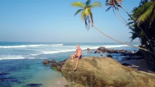 Hombre Bronceado Descansando Sienta Roca Alta Playa Azul Del Océano — Vídeo de stock