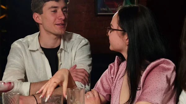 Brunette woman in glasses runs finger over glass flirting with guy. Young man looks at woman with interest during conversation