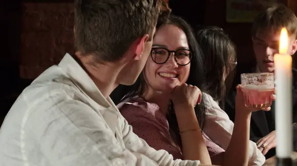 Cheerful couple communicates on romantic date with alcoholic cocktail. Young people laugh during emotional conversation at night bar