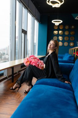 Rahat genç bayan, personel odasındaki bir buket çiçekle kanepede oturuyor. Kadın çalışan terfiyi kutlamak için çiçek alıyor