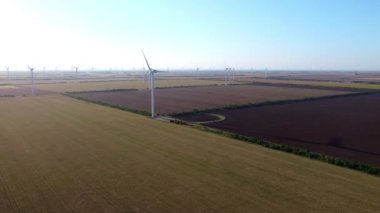 Büyük pervaneli yel değirmenleri güneşli havada tarım alanında döner. Çağdaş jeneratörler kırsal alanda yenilenebilir enerji üretiyorlar
