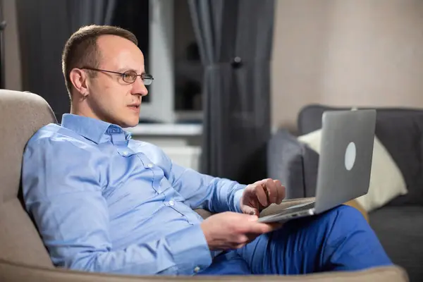 公司的男性心理学家坐在轻松的扶手椅上 看着笔记本电脑的屏幕 穿着蓝色衬衫的有魅力的男性会咨询在职员工 图库图片