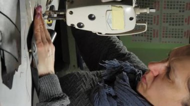 Kadın terzi atölyedeki makineyi kullanarak deri telefon kılıfı dikiyor. Odaklanmış kadın dikkatli bir şekilde kenar işleyerek kaliteli dikişler atıyor.