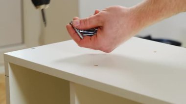 İnsan elleri, raflardaki deliklere vida yerleştirmek için elektrikli tornavida kullanır. Tamirci, modern prefabrik mobilyaların montajını yapıyor.