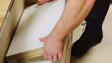 Adam beyaz kontrplak detaylarını karton kutudan çıkarıyor. Erkek işçi, montaj işlemine hazırlanan prefabrik mobilyaların parçalarını dikkatlice açıyor