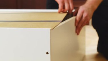 Adam mobilya parçalarını birleştiriyor ve detayları bağlamaya hazırlanıyor. İşçi beyaz kontraplaktan şifoniyer hazırlar. Vidaları için delikleri kontrol eder.