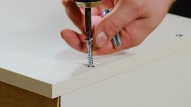 Erkek elleri beyaz kontrplak şifoniyer deliğine elektrikli tornavidayla vida takar. Tamirci ayrıntıları mobilya yüzeyine zarar vermeden dikkatlice bağlar