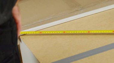 Tamirci bant kullanarak şifoniyer ahşap parçasının ölçüsünü alıyor. Prefabrik mobilyalar için uygun parçalar yapmak için boyutları ölçmek için temel araç