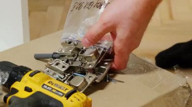 Erkek eli plastik torbadan metal menteşeleri çıkarır karton kutuya koyar. Tamirci, kabine kapısının birleştirme işlemleri için elementleri hazırlıyor