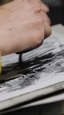 Yaratıcı, ders sırasında fırçayla kağıt yaprağına boya uygular. Sanatçı fırça darbeleri uyguluyor ve stüdyoda figür oluşturan renklere doygunluk ekliyor