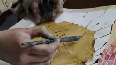 Kadın sanatçı kahve tekniğini kullanarak resim yapmayı öğreniyor. Sanatçı doku üzerinde çizgiler oluşturur ve boya şişesi kullanarak elementin hatlarını temizler.