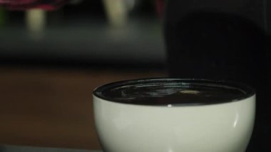 Kadın, fincanın üstündeki fazla sıvının kaymağını yemek için bir çay kaşığı kullanıyor. Barista kahve kalıpları döküyor kaşık sallayarak su havzasında ağır çekimde