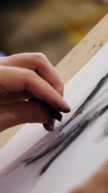 Adam mangal kömürüyle çizer ve beyaz kağıt üzerine çizgileri yumuşatır. Sanatçının çalışmasının dokunsal süreci gölgeleme ve yumuşatma tekniklerini gösterir