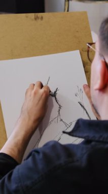 Adam ahşap tahtaya tutturulmuş beyaz kağıda resim çiziyor ve manken çizimi yapıyor. Yaratıcı süreç ve aracın hassas uygulaması