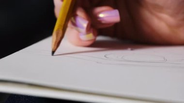 Sanatçı elinde kağıt üzerinde resim çizimi yapıyor. Bayan çizim ve malzeme yüzeyine kalemle dokunur.