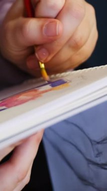 Kırmızı fırçayı elinde tutan kişi spiral çizim defterine mor boya sürüyor. Canlı renkler ve dinamik fırça izleri sanatsal yaratımı öneriyor