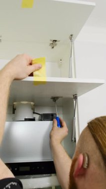 İşitme engelli bir adam mutfaktaki bantla kapıyı tutarken menteşe takıyor. İşçi egzoz kaputu dikey çekim üzerine kabine monte