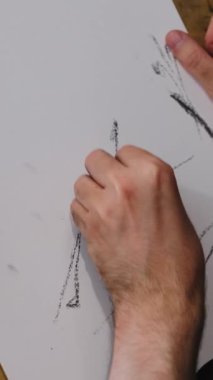 Erkek el, yüzeyinde belli belirsiz çizgiler olan beyaz kağıt üzerinde izler yaratmak için aktif olarak koyu renk çizim aracı kullanır. Stüdyoda çizim süreci