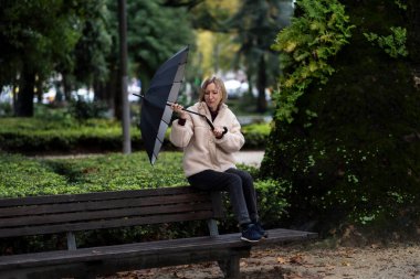 Parktaki bankta oturan bir kadın. Yağmurlu havada bir şemsiye kırıldı.