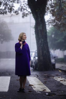 Sonbahar montu giymiş şık bir kadın sabah sisinin içinde dışarıda duruyor.. 