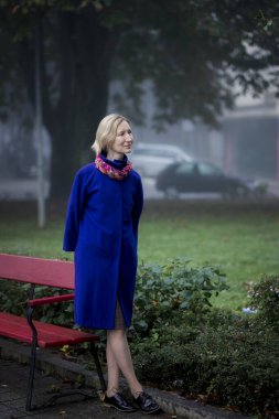 Sonbaharda sarışın bir kadın parktaki bankta duruyor..