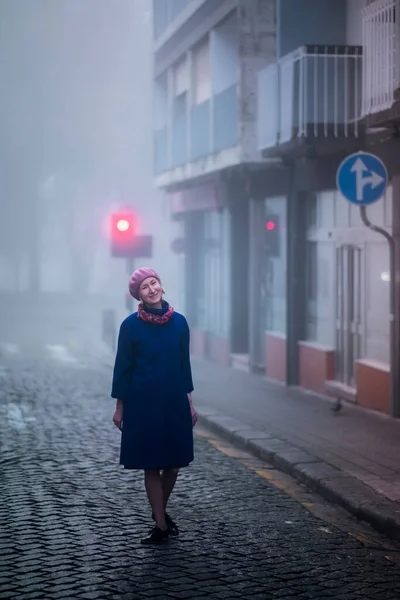清晨的雾中 一个穿着大衣的金发女人站在人行道上 — 图库照片