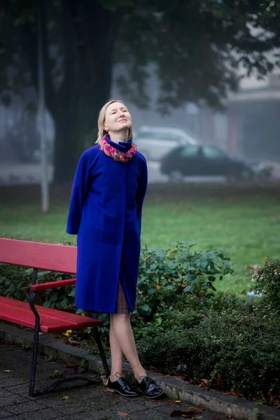 Μια Ξανθιά Γυναίκα Ένα Μπλε Φανταχτερό Παλτό Στέκεται Ένα Πάρκο — Φωτογραφία Αρχείου