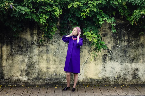 一个穿着淡紫色外套和贝雷帽的女人站在墙边的人行道上 — 图库照片