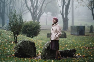 Sisli bir sonbahar sabahında bir kadın parkta yürüyor.