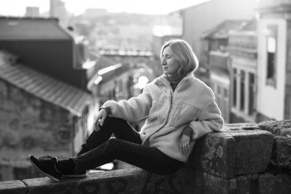 葡萄牙波尔图 一名女游客坐在石墙上 背景中的房子模糊不清 黑白照片 — 图库照片