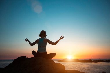 Nilüferde yoga yapan bir kadın gün batımında sahilde meditasyon yapıyor..