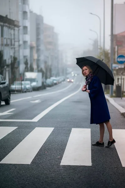 曇りの日に傘を差した女性が道路脇に立っている — ストック写真