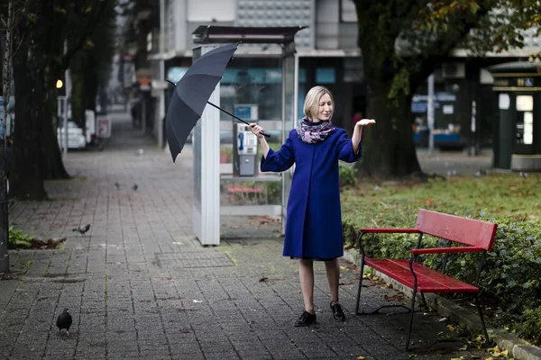 A woman with an umbrella on the street realizes that the rain has stopped.
