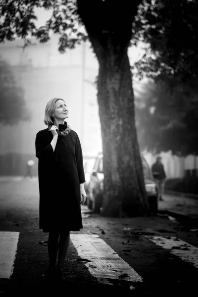 在城市的人行道上站着一位穿着秋衣的妇女 黑白照片 — 图库照片