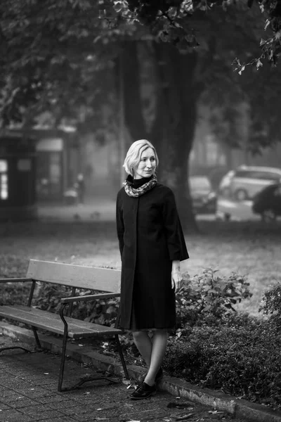 一个穿着外套的女人站在公园的长椅旁边 黑白照片 — 图库照片