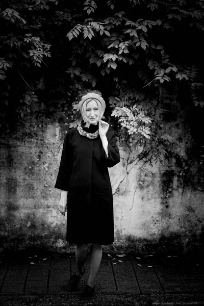 一个穿着秋衣的女人站在石墙旁边的人行道上 黑白照片 — 图库照片