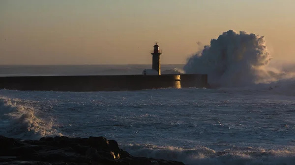 Wave on the lighthouse in the background on the sunset. Atlantic, Porto, Portugal.