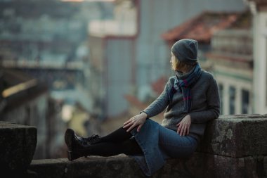 Portekiz 'in Porto şehrinde antik bir taş duvarda bir kadın oturuyor..